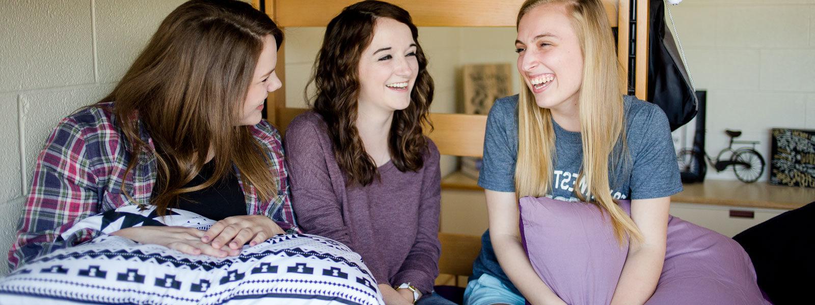 three female students sitting on bunk bed in dorm room